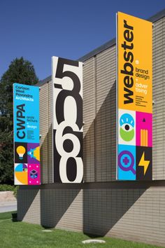 several banners on the side of a building with grass and trees in the foreground