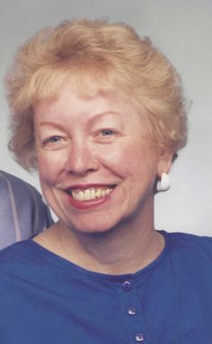 an older woman with blonde hair smiling at the camera while wearing a blue shirt and earrings