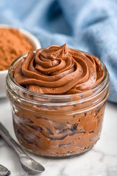 a glass jar filled with chocolate frosting next to spoons