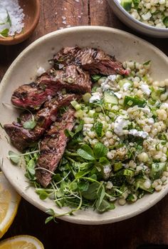 a bowl filled with meat and vegetables next to two bowls of lemon wedged salad