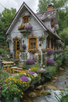 a small house with flowers on the windows and balcony above it is next to a stream