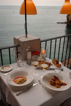 two plates of food on a table with wine and silverware in front of the ocean