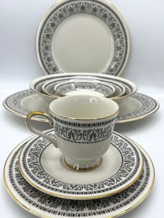 a white and black dinner set with gold trimmings on the rim, in front of a white background