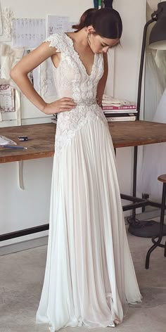 a woman standing in front of a table wearing a white dress with lace on it