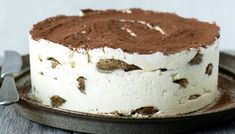 a cake with white frosting and chocolate toppings on a plate next to a knife