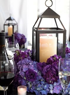 a candle and some purple flowers are on a table with wine glasses in front of it