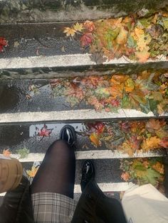 the legs and feet of a person who is standing on some steps with leaves all over them