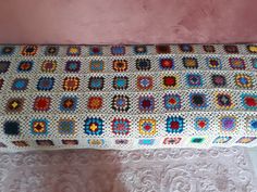 a crocheted blanket is laying on top of a white doily next to a pink wall