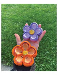 a person holding two flower shaped objects in their hand on top of green grass covered ground