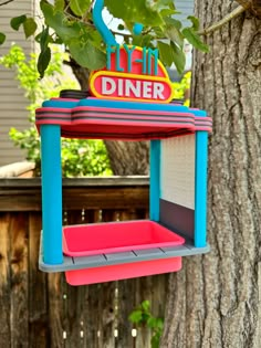 a colorful bird feeder hanging from a tree in front of a house with a sign that says flyin'diner on it