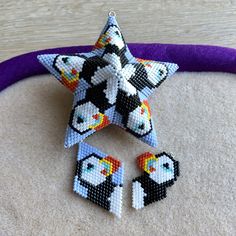 the beaded star is next to two small penguin earrings on top of a purple pillow