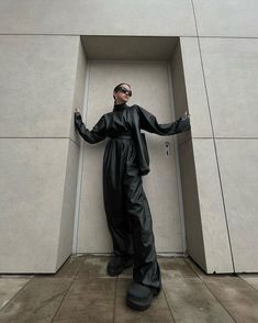 a man standing in front of a wall with his hands on his hips wearing sunglasses