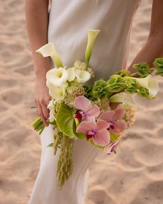 a bride holding a bouquet of flowers on the beach