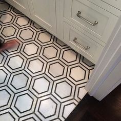 a bathroom with white cabinets and black and white floor tiles on the floor, while someone is using a vacuum cleaner to clean it