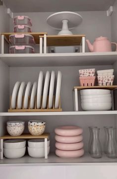 the shelves are filled with dishes, cups and other kitchen wares in pink and white