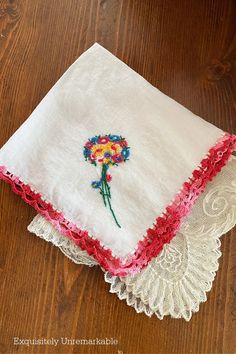 two white handkerchiefs with colorful flowers on them sitting on a wooden floor next to a lace doily