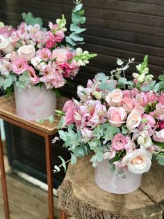 two vases filled with pink and white flowers on top of a wooden table next to a wall