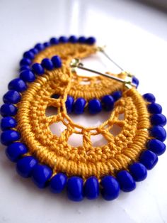 a pair of blue and yellow earrings on a white surface with gold accents, one bead in the shape of a circle