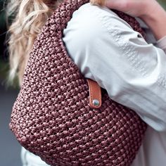 a woman carrying a brown crocheted purse on top of her shoulder and wearing a white shirt