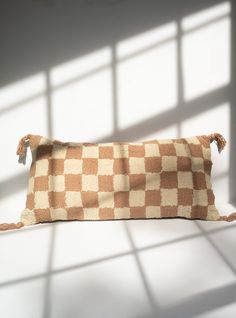 a brown and white checkerboard pillow sitting on top of a table next to a window