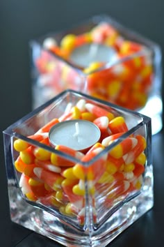 two clear cubes filled with candy corn and a lit candle on the top one