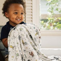 a little boy that is sitting down with a blanket on his chest and smiling at the camera