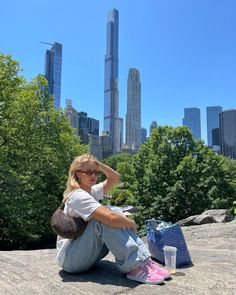 a woman sitting on top of a rock next to a blue bag and some trees