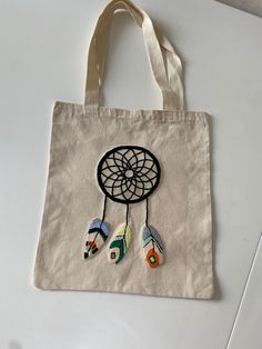 a tote bag with an embroidered dream catcher on the front and two feathers hanging from it