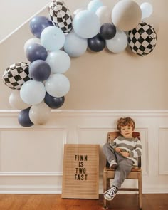 a young boy sitting in a chair next to a bunch of balloons