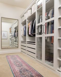 a walk in closet filled with lots of white shelves and drawers next to a rug