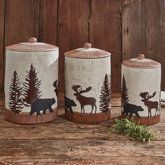 three ceramic canisters with moose and pine trees painted on them, sitting on a wooden surface