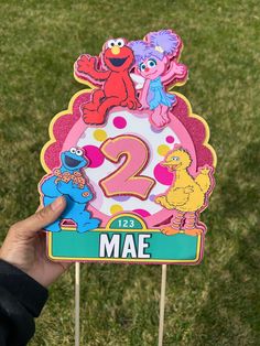 someone holding up a sesame street sign with the number two on it in front of some grass