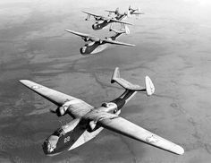 four planes flying in the sky above water and land area, with one plane upside down