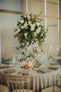 the centerpieces on this table are filled with white flowers and greenery as well as candles