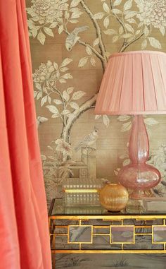 a pink lamp sitting on top of a table next to a wallpapered wall