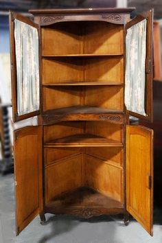 an old wooden corner cabinet with curtains on the top and doors open to reveal it's contents