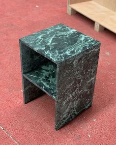 a green marble side table sitting on top of a red carpeted floor next to two wooden benches