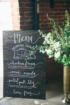 a menu board with flowers in it next to a vase filled with white flowers and greenery