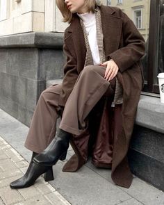 a woman sitting on the side of a building with her legs crossed and wearing black boots