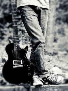 black and white photograph of a person holding an electric guitar in their right hand while standing on the ground