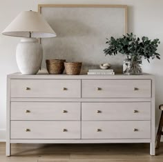 a white dresser with two vases on top and a lamp next to it in a room