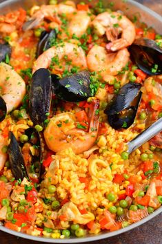 a pan filled with seafood and rice on top of a wooden table