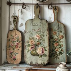 three wooden cutting boards with flowers painted on them, hanging from a wall above a dresser