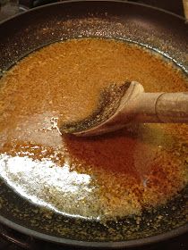 a wooden spoon in a frying pan filled with brown liquid and spices on the stove