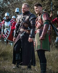 two men dressed in medieval armor standing next to each other on a grass covered field