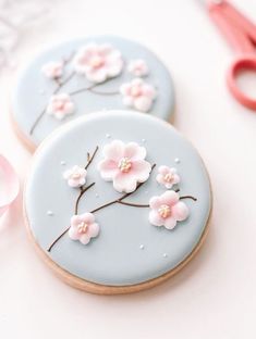 two decorated cookies sitting on top of a table next to scissors and pink flowers in the middle