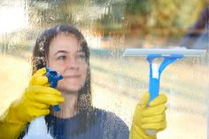 a woman in yellow gloves holding a blue and white toothbrush while looking through a window