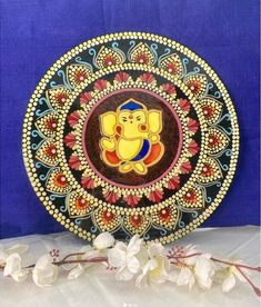 a decorative plate with an image of lord ganesha on it and flowers in the foreground