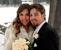 a bride and groom posing for a photo in the snow with their fur coat over their shoulders