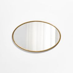 an oval mirror with gold rim on a white wall